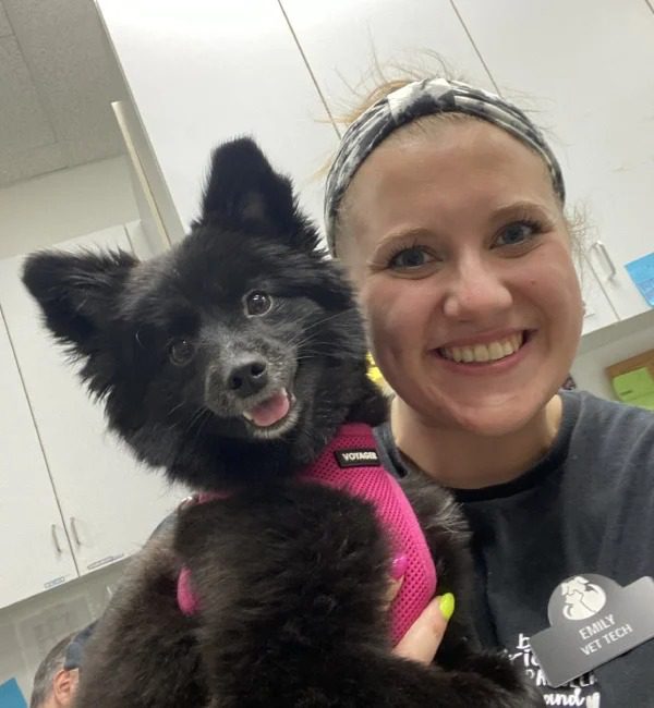 Emily smiling while holding her small black dog